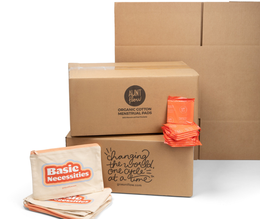 Cardboard boxes with 'Aunt Flow' and 'Basic Necessities' branding on a white background