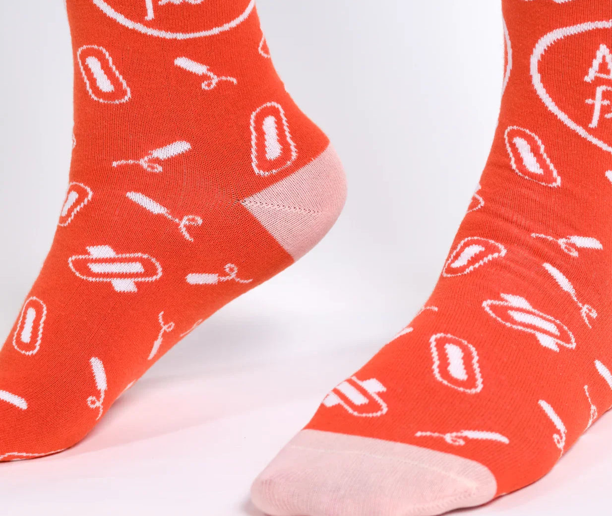 A pair of orange socks with white text and graphics, including the phrase 'Aunt flow' and menstrual-themed icons.