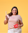 Model wearing Aunt Flow "Changing the World, One Cycle at a Time" peach colored t-shirt. Posing with Aunt Flow Cartridge Tampon and Pad